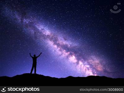 Night colorful landscape with purple Milky Way and silhouette of a standing sporty man with raised up arms on the mountain. Sky full of stars, space.