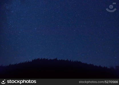 Night dark blue sky with many stars and milky way galaxy above a mountain