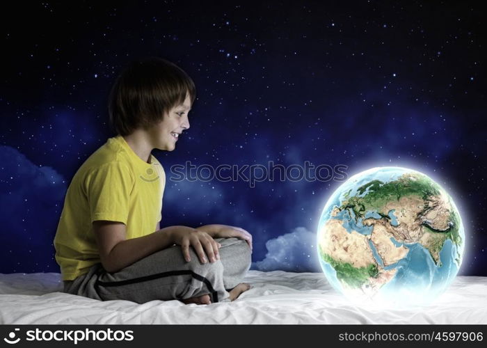 Night dreaming. Cute boy sitting in bed and dreaming. Elements of this image are furnished by NASA