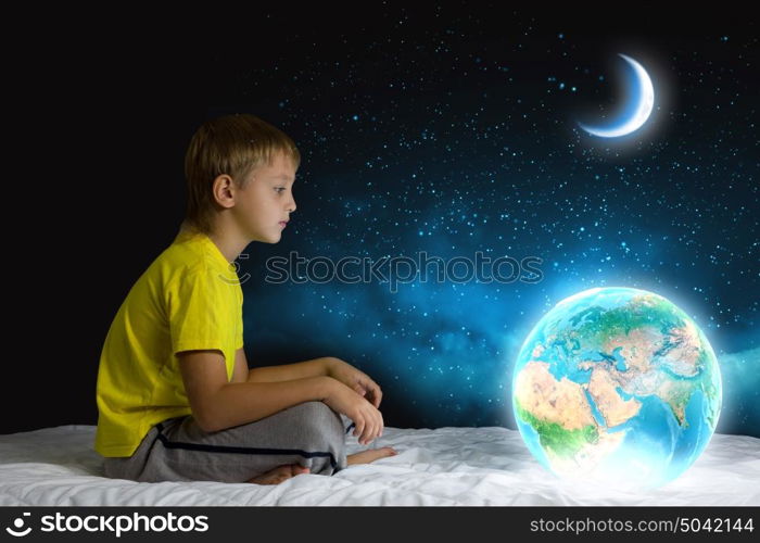 Night dreaming. Cute boy sitting in bed and dreaming. Elements of this image are furnished by NASA