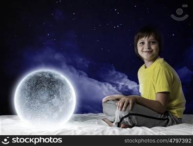 Night dreaming. Cute boy sitting in bed and dreaming about moon