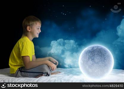 Night dreaming. Cute boy sitting in bed and dreaming about moon