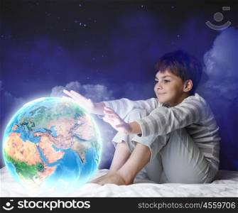 Night dreaming. Cute boy sitting in bed and looking at Earth planet. Elements of this image are furnished by NASA
