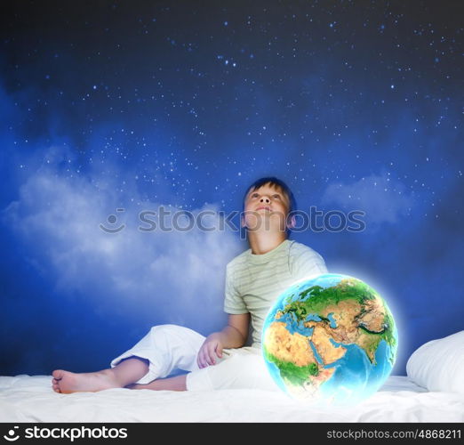 Night dreaming. Cute boy sitting in bed and looking at Earth planet. Elements of this image are furnished by NASA