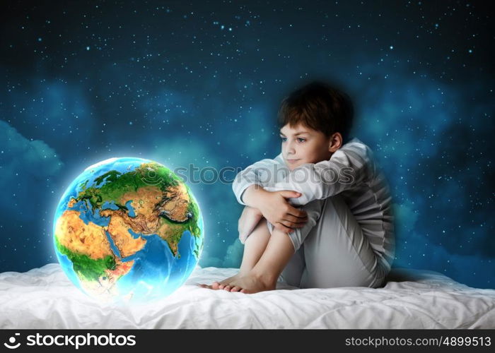 Night dreaming. Cute boy sitting in bed and looking at Earth planet. Elements of this image are furnished by NASA