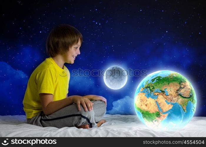 Night dreaming. Cute boy sitting in bed holding Earth planet. Elements of this image are furnished by NASA