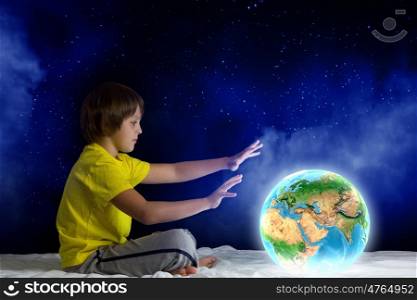 Night dreaming. Cute boy sitting in bed holding Earth planet. Elements of this image are furnished by NASA