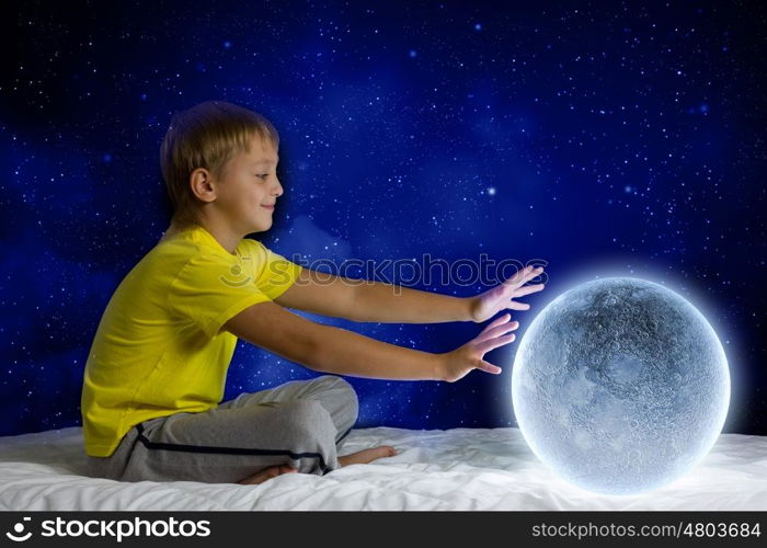 Night dreaming. Cute boy sitting in bed with moon planet