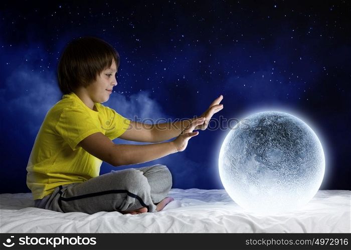 Night dreaming. Cute boy sitting in bed with moon planet