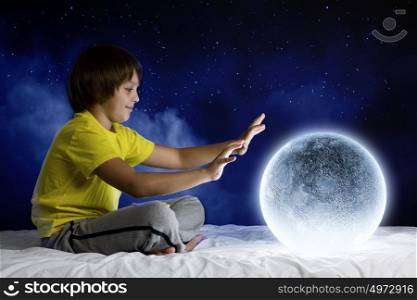 Night dreaming. Cute boy sitting in bed with moon planet