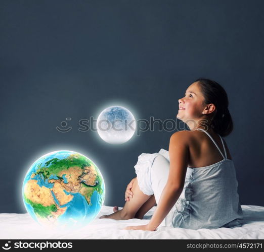 Night dreaming. Cute girl sitting in bed and looking at Earth planet. Elements of this image are furnished by NASA