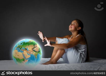 Night dreaming. Cute girl sitting in bed and looking at Earth planet. Elements of this image are furnished by NASA