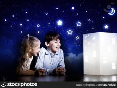 Night dreaming. Cute little boy and girl looking at model of house