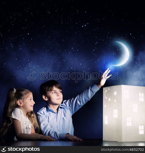 Night dreaming. Cute little boy and girl looking at model of house