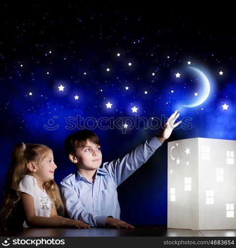 Night dreaming. Cute little boy and girl looking at model of house