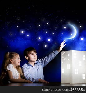 Night dreaming. Cute little boy and girl looking at model of house