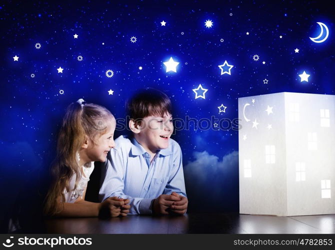 Night dreaming. Cute little boy and girl looking at model of house