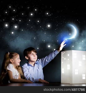 Night dreaming. Cute little boy and girl looking at model of house