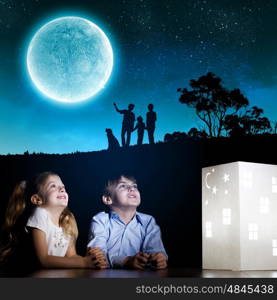 Night dreaming. Cute little boy and girl looking at model of house