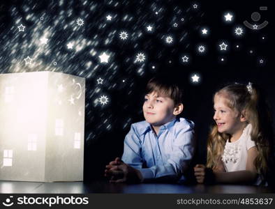 Night dreaming. Cute little boy and girl looking at model of house