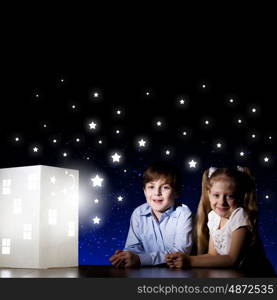 Night dreaming. Cute little boy and girl looking at model of house