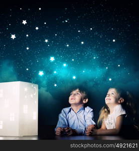 Night dreaming. Cute little boy and girl looking at model of house