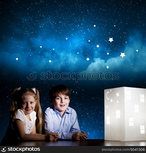 Night dreaming. Cute little boy and girl looking at model of house