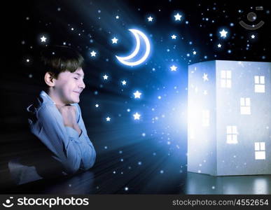 Night dreaming. Cute little boy looking at model of house