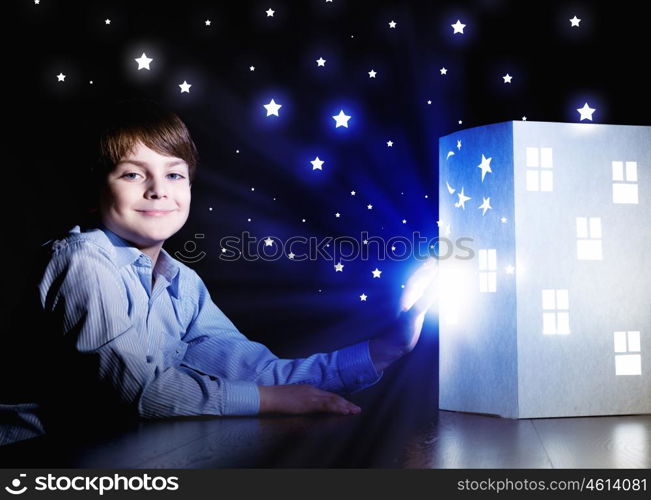 Night dreaming. Cute little boy looking at model of house