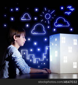 Night dreaming. Cute little boy looking at model of house