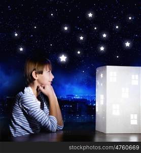 Night dreaming. Cute little boy looking at model of house