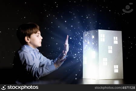 Night dreaming. Cute little boy looking at model of house