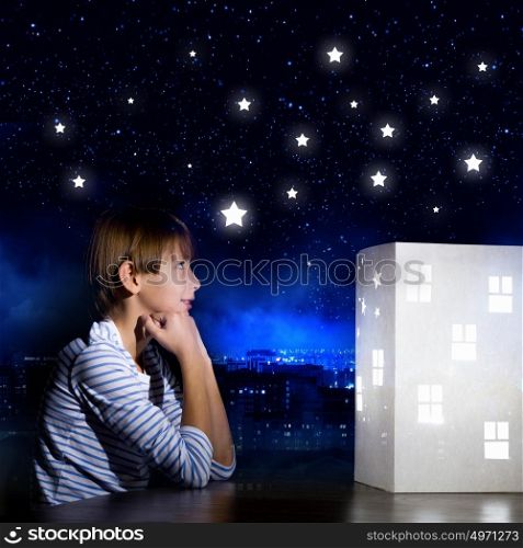 Night dreaming. Cute little boy looking at model of house