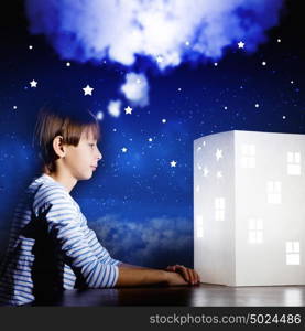 Night dreaming. Cute little boy looking at model of house