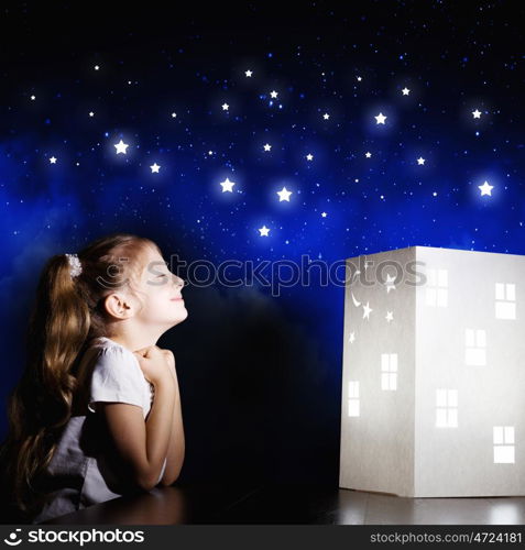 Night dreaming. Cute little girl looking at model of house and dreaming