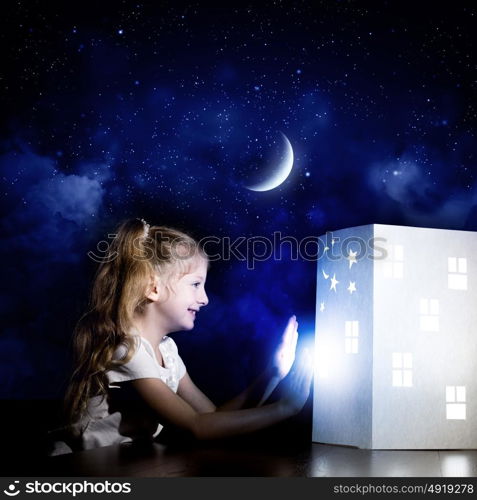 Night dreaming. Cute little girl looking at model of house and dreaming