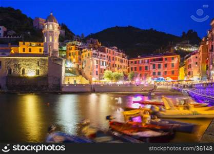 Night fishing village Vernazza with Santa Margherita di Antiochia Church, Five lands, Cinque Terre National Park, Liguria, Italy. Boats blurred motion on the foreground.