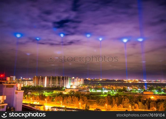 Night illuminated city with blue lights in the clouds and sky