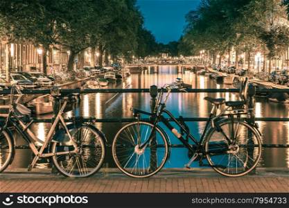 Night illumination of Amsterdam canal and bridge with typical dutch houses, boats and bicycles, Holland, Netherlands.. Toning in cool tones