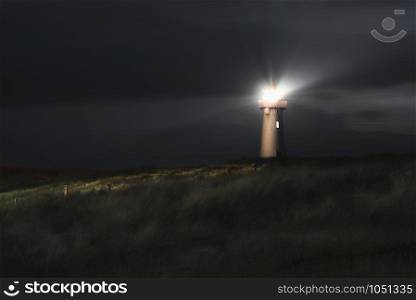 Night landscape with a lighthouse on dunes with high grass, on Sylt island, on North sea coastline Germany. Beacon on dune. German lighthouse at night