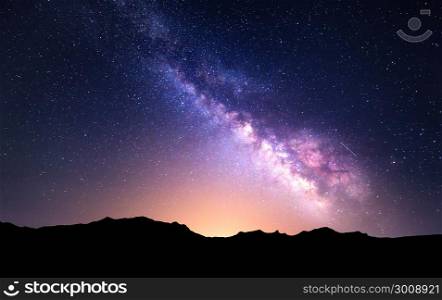 Night landscape with colorful Milky Way and yellow light at mountains. Starry sky with rocks at summer. Beautiful Universe