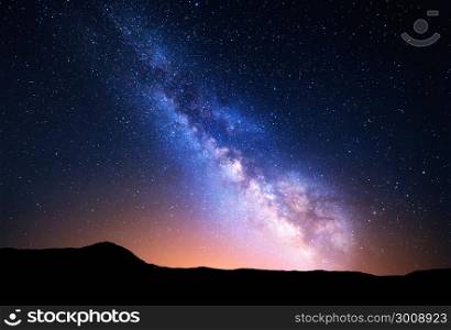 Night landscape with colorful Milky Way and yellow light at mountains. Starry sky with rocks at summer. Beautiful Universe