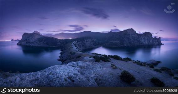 Night landscape with mountains, sea, starry sky and city lights. Amazing view with rocks at dusk in Crimea