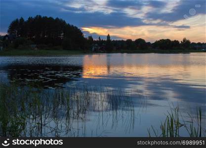 Night landscape with reflection of sunset in a lake in the countryside. View of distant silhouettes of trees and houses. Lake Seliger, Russia. Selective focus.