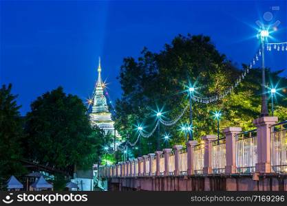 Night of Evening walk light on the foot bridge and bright illumination of chedi at Wat Ket Karam is a Buddhist temple is a major tourist attraction in Chiang Mai,Thailand.at twilight time blue sky.