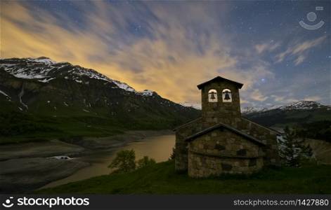 Night photography of a landscape of the Alps. Lake with stars in the sky and moving clouds. Church in the mountain