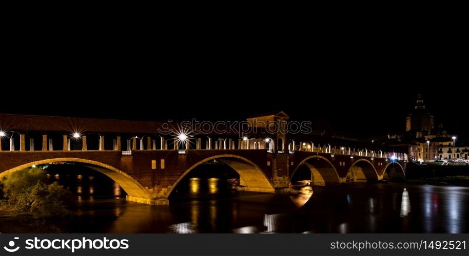 Night photography of the Ponte Coperto of Pavia, historical building also called Ponte Vecchio built on the Ticino river. Horizontal image of Italian night landscape.