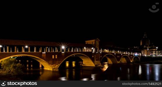 Night photography of the Ponte Coperto of Pavia, historical building also called Ponte Vecchio built on the Ticino river. Horizontal image of Italian night landscape.