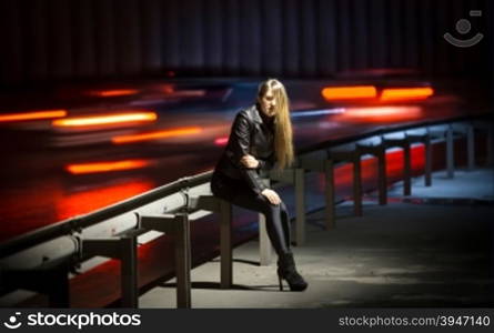 Night scene of sexy young woman posing at highway with blurred car lights