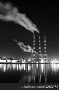 Night shot of Industrial smoke stacks reflecting on water.
